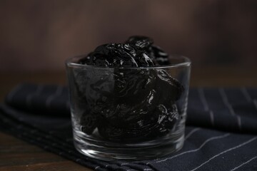 Tasty dried plums (prunes) in glass bowl on wooden table, closeup