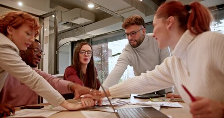 Cheerful corporate colleagues celebrating by putting their hands together in a bright workspace, embodying teamwork and achievement.