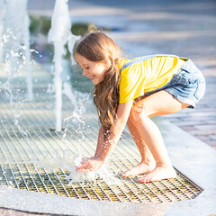 A happy little girl has fun near the city fountain. The child has a rest near a fountain during a heat wave. Summer vacation concept