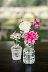 Assorted flowers in glass vases on dark wooden table outdoors

