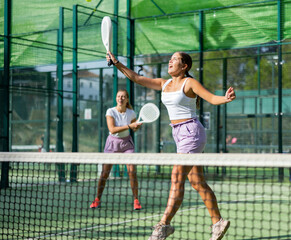 Young woman in shorts jumping while playing padel tennis on court. Racket sport training outdoors.