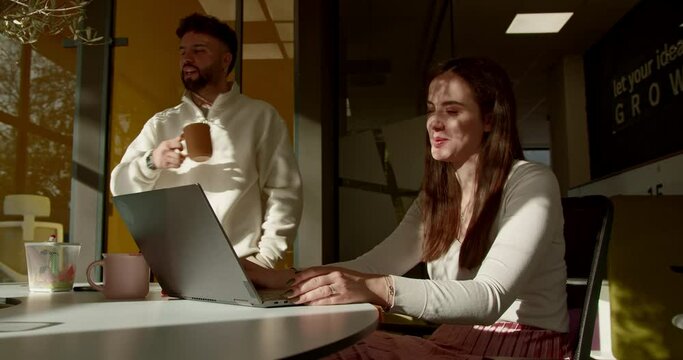 In a positive atmosphere at the office, business colleagues work together on a project, engaging in discussions, sharing jokes, and laughing, fostering a productive and enjoyable work environment.