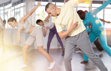 Dynamic young guy training hip-hop dance poses in dancehall during workout session
