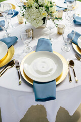 Elegant table setting with gold plates, blue napkins, and white flowers.

