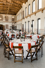Rustic reception hall with decorated round tables and wooden chairs

