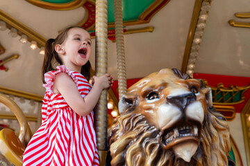 Adorable little brunette girl in summer red-white dress at amusement park having a ride on the...