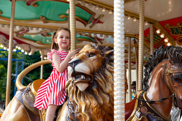 Adorable little brunette girl in summer red-white dress at amusement park having a ride on the...