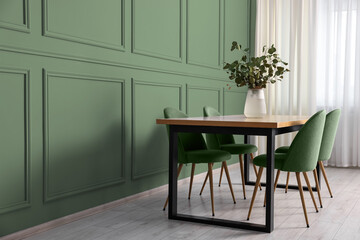Dining table with chairs near sage green wall indoors. Interior design