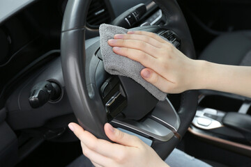 Naklejka premium Woman cleaning steering wheel with rag in car, closeup