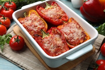 Tasty stuffed peppers in dish and ingredients on light blue wooden table