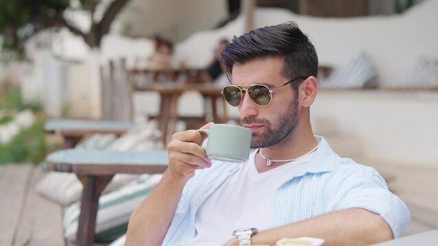 Happy Caucasian man enjoy outdoor lifestyle travel tropical island on summer beach holiday vacation. Handsome guy relaxing and drinking coffee at beach cafe and looking beautiful nature of the sea.
