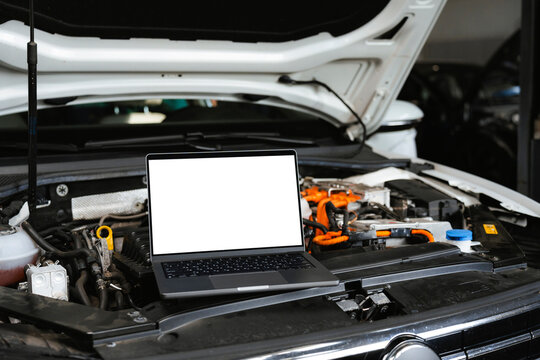 A laptop with white screen under the open car hood  
