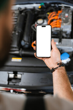 A man uses a mobile phone with white screen in a car repair shop