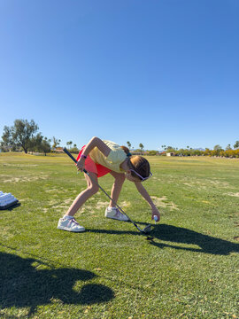 Young Girl puts ball on tee on practice golf  range 