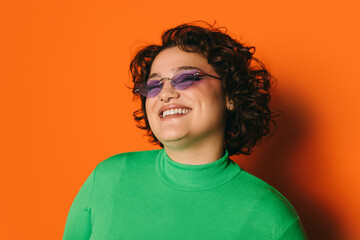 Joyful young curvy woman in purple sunglasses on orange background