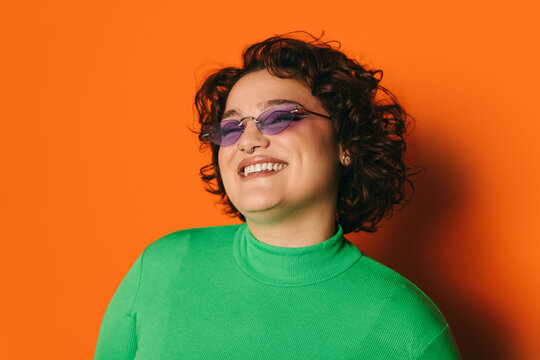 Joyful young curvy woman in purple sunglasses on orange background