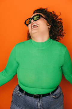 Joyful curvy woman in green laughing against orange background