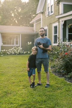 father and son holding black kitten while standing in front of home