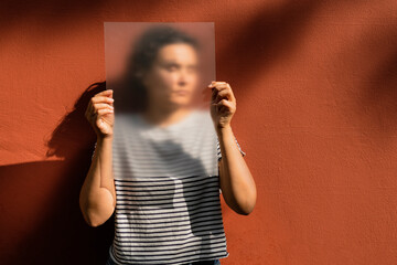 Woman with short curly hair holding frosted acrylic sheet over face