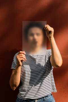 Woman with short curly hair holding frosted acrylic sheet over face