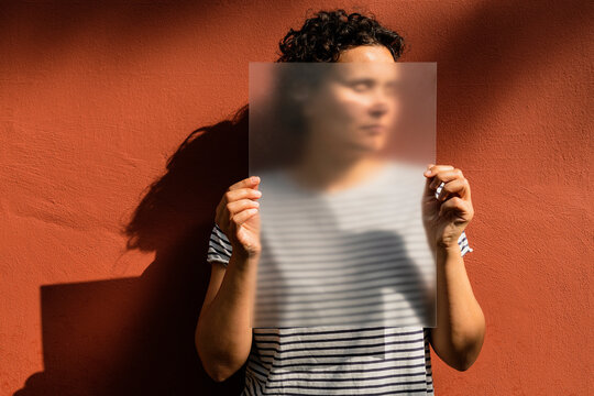 Woman with short curly hair holding frosted acrylic sheet over face