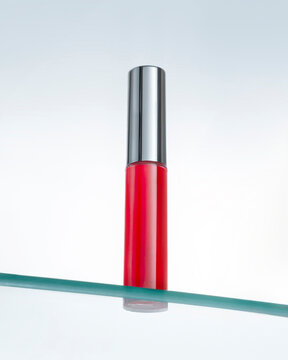 Red lipgloss with glossy cap on glass sheif in hero view perspective.