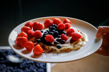 pancakes adorned with ripe red strawberries and juicy blueberries, complemented by a luscious cream topping.