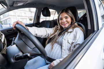 Smiling pregnant woman driving car