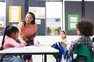 A biracial teacher helping group of biracial students in classroom