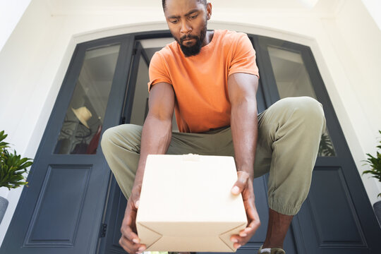 African American young man in casual clothes picking up package from his doorstep, at home