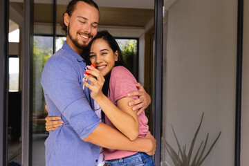 Diverse young couple hug and smile while holding a key, buying first home