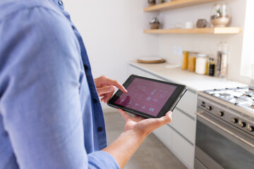 Young Caucasian man using smart home app on tablet in a modern kitchen