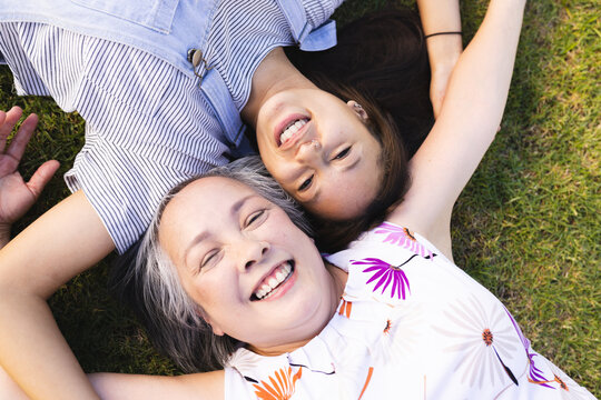 Asian grandmother and biracial granddaughter lying on grass smiling together
