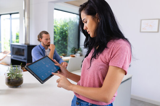 Young biracial woman using tablet with smart home app, caucasian man working on laptop - Powered by Adobe