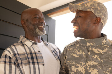 African American father and soldier son smiling at each other, soldier son wearing military uniform