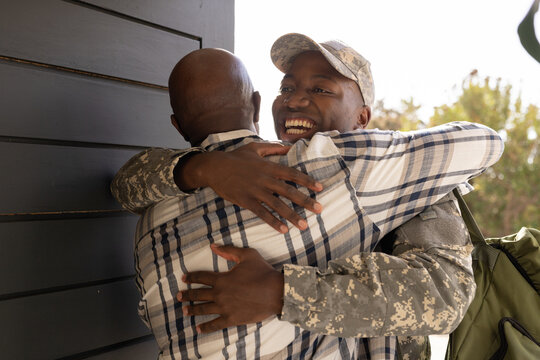 Young African American soldier in military uniform hugging older soldier warmly - Powered by Adobe