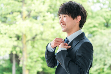 新緑の中にいる若いスーツ姿のビジネスマン・新入社員・転職・就職活動

