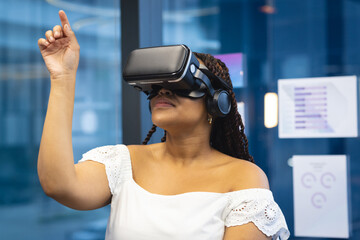 A biracial young woman in a VR headset raises her hand to interact in an business office