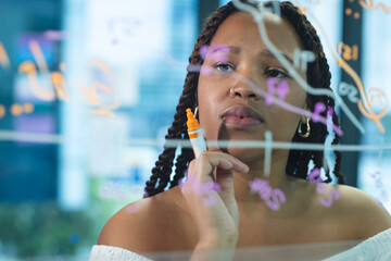 Young biracial woman writing on a transparent board with a marker in the business office