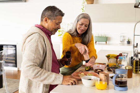 A biracial mature couple prepares meal together in a bright kitchen, at home