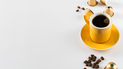 Yellow coffee cup with golden coffee capsules and beans on a white background. Copy space