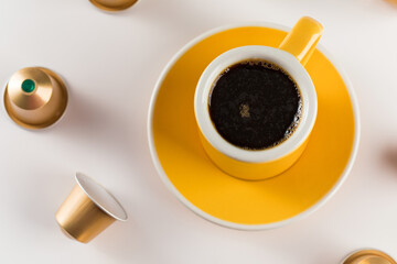 Yellow coffee cup with golden coffee capsules on a white background.