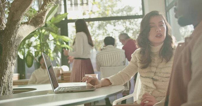 Business colleagues having a casual meeting in a modern office. People are engaged in conversation and working on laptops, creating a collaborative work environment.
