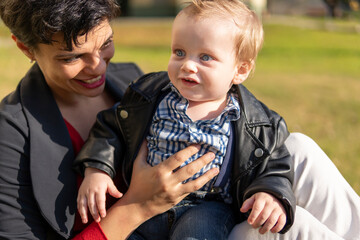 Portrait of blue-eyed blonde baby in the park with his mother