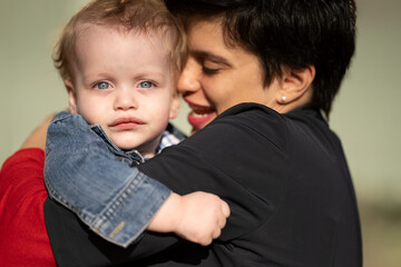 Close-up portrait of blue-eyed blonde baby looking at camera in his mother's arms