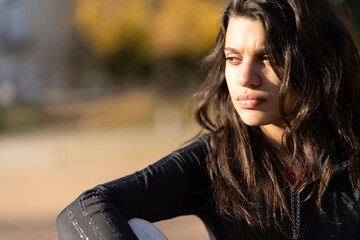 Close up portrait of teenage girl with thoughtful expression sitting in the park
