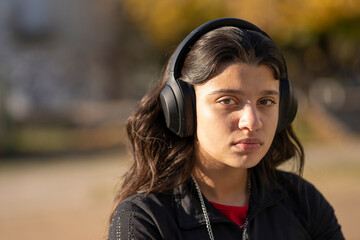 Teenage girl sitting in a park with a worried expression and a lost look while holding headphones