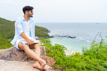 Caucasian man sitting on mountain peak remote working online corporate business financial on laptop computer. People enjoy outdoor lifestyle travel tropical island on summer beach holiday vacation.