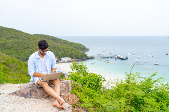 Caucasian man sitting on mountain peak remote working online corporate business financial on laptop computer. People enjoy outdoor lifestyle travel tropical island on summer beach holiday vacation.