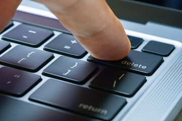 Finger of the computer user, he presses the delete button on the computer keyboard.	
